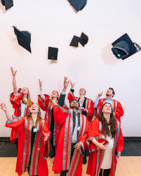 PhD graduates in red academic gowns celebrate by tossing their mortarboards into the air during the IGSN graduation ceremony.